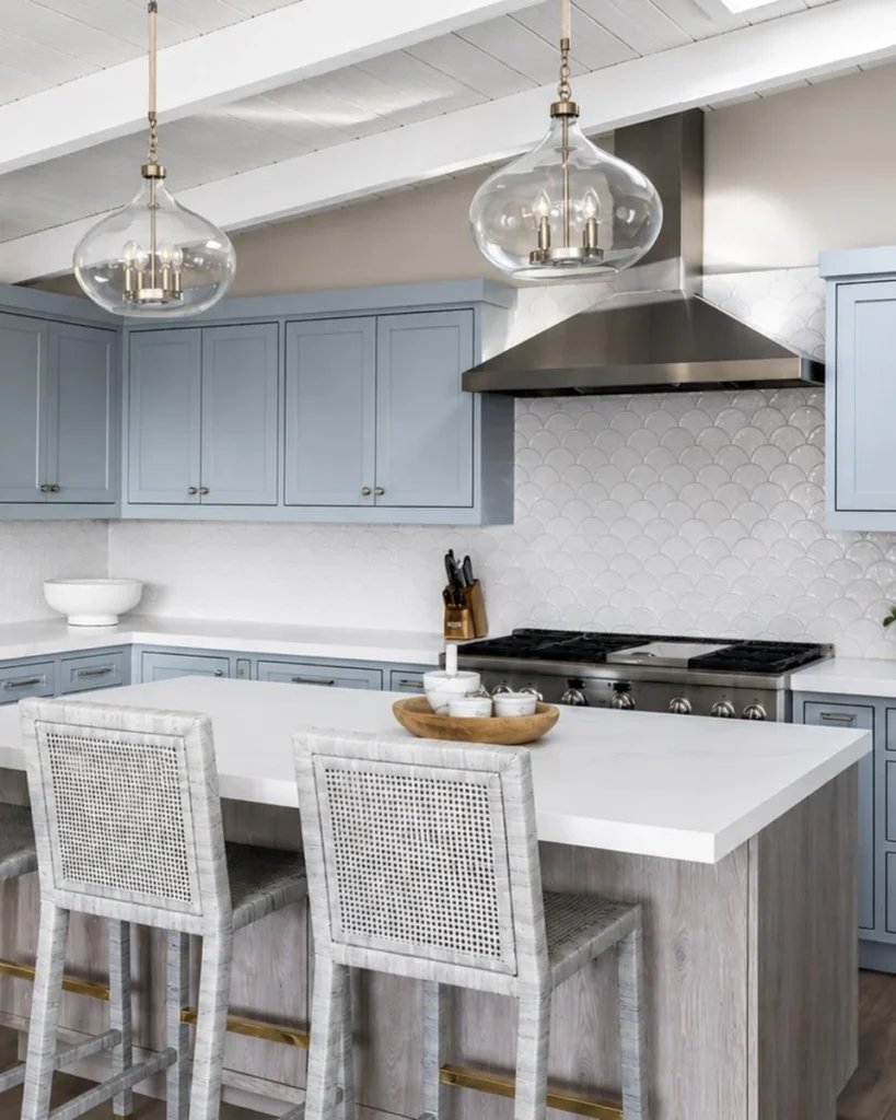 Pale blue shaker, white scallops, and a hood the same finish as the range. Nothing in this kitchen is fighting anything else.